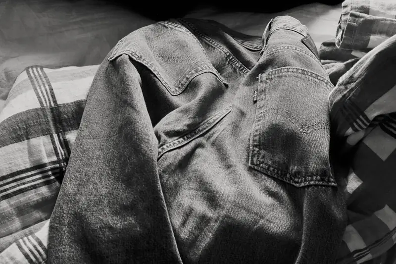 Close-up of a pair of Levi's denim jeans resting on patterned fabric. The back pockets and the small Levi's tag are clearly visible against the coarse denim texture.