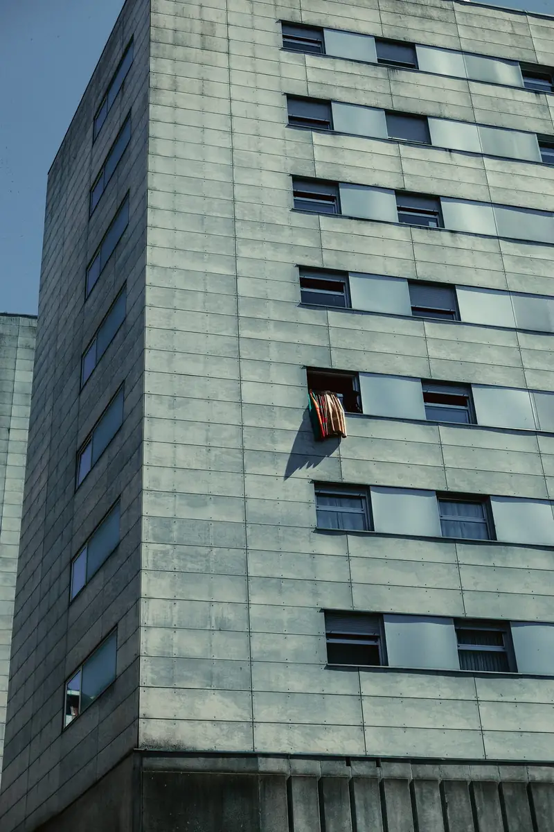 A grey apartment building in Bilbao with a grid of windows. Red, green and orange laundry hangs from one open window on an otherwise bare concrete facade.